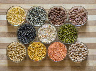 Twelve bowls of lentils and legumes on a chopping board