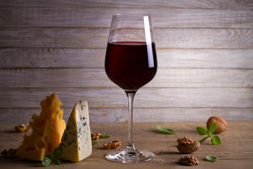 Red wine and cheese on wooden table background. Cheese appetizer selection or wine snack set. Glass and bottle of wine