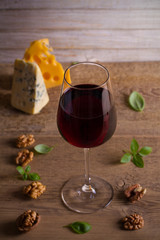 Red wine and cheese on wooden table background. Cheese appetizer selection or wine snack set. Glass and bottle of wine