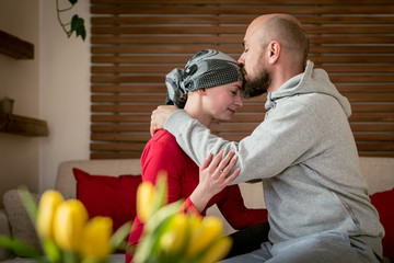 Supportive husband kissing his wife, cancer patient, after treatment in hospital. Cancer and family support concept.
