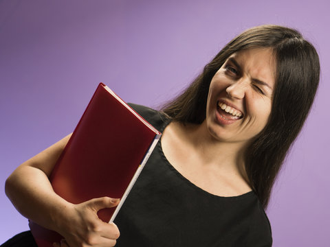 Young Woman in Black Dress with Red Notebook on Purple Background. Employee Girl Winking with Folder of Documents. - Powered by Adobe
