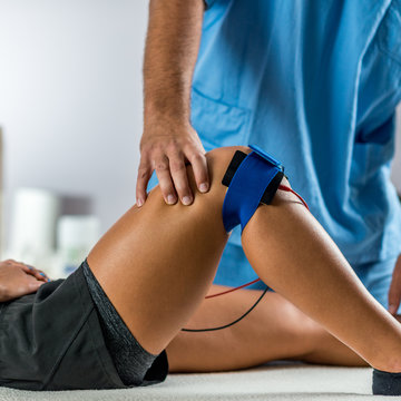 Electrical stimulation in physical therapy. Therapist positioning electrodes on a patient's knee