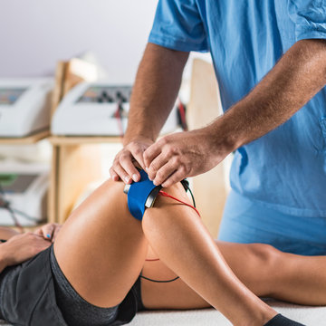 Electrical stimulation in physical therapy. Therapist positioning electrodes on a patient's knee