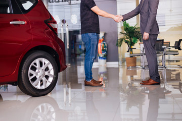 Businessman in formal suit handshaking with other partner in car background in showroom - successful partnership and deal concept.