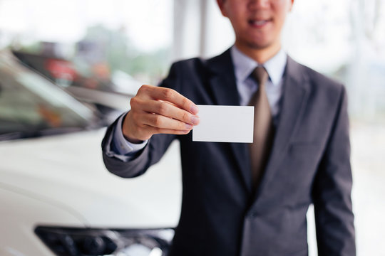 Smiling and happy businessman in formal suit presenting and showing an empty namecard with the car in scene background - with copyspace ready to put text on.