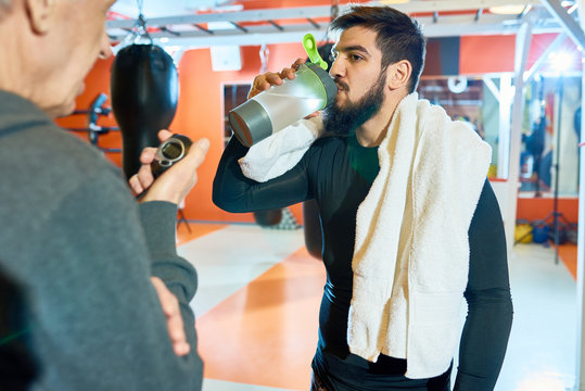 Waist up portrait of bearded Middle-eastern man drinking water after tough training in martial arts club, copy space
