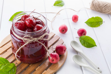 Glass jar of  small paradise apple jam with fresh fruits on white table.