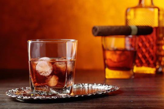 Glass of scotch whiskey with natural ice and cigar .