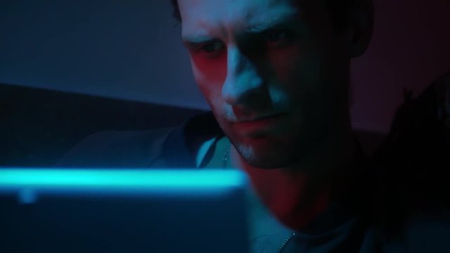 4k Retro wave hacker works with laptop in dark cold light room close-up
