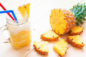 Pineapple smoothie in glass jar and sliced pineapple on wooden table