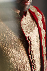Portrait of attractive Indian groom dressed in red sherwani with golden design
