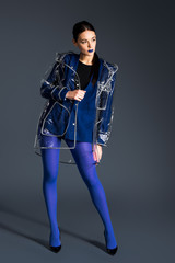 Young girl with blue lipstick wearing transparent raincoat on dark background