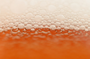 Bubbles from a beer froth close-up on half a glass.