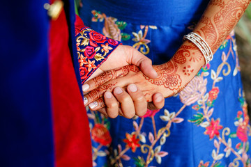 Fototapeta na wymiar Indian groom holds bride's arm with henna tattoo tender