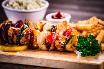Kebabs - grilled meat with french fries and vegetables on wooden background