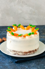 Carrot cake with cream cheese frosting decorated with carrot marmalade serving on a plate on a blue stone background.