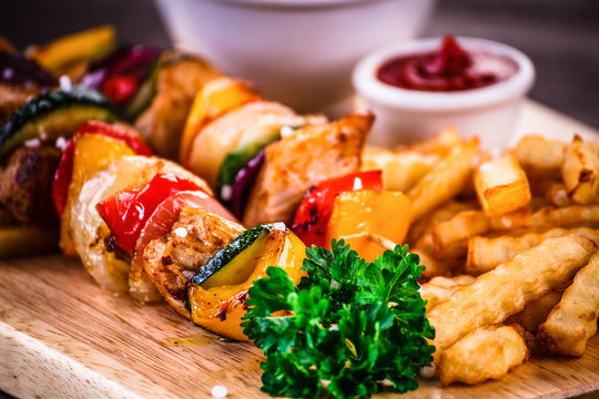 Kebabs - grilled meat with french fries and vegetables on wooden background