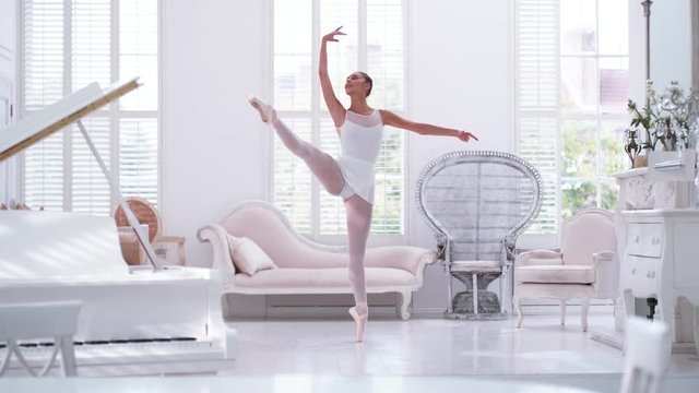 Graceful ballerina practicing ballet in white studio, slow motion