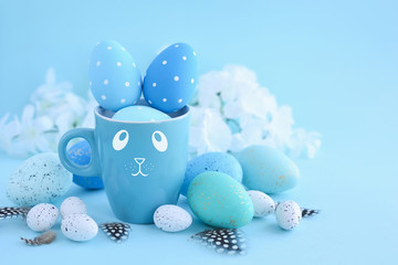 Easter eggs and a cup in the form of a rabbit on a blue background. Easter card with empty space for text