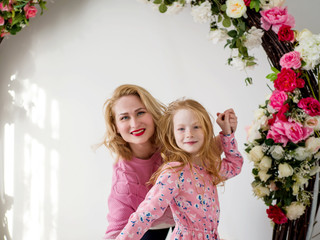 Beautiful mother and red-haired daughter stand in an embrace against the background of flowers in the studio