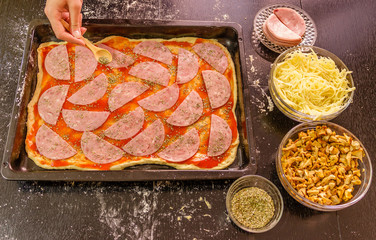 Preparing homemade pizza with cheese,salami, mushrooms and oriegano on black wooden table