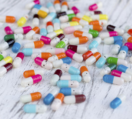 Assorted pharmaceutical medicine pills. Colorful capsules with emotions over white wooden background