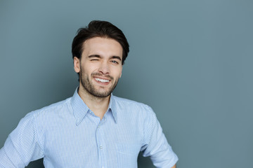 Non verbal language. Cheerful positive happy man smiling and winking while looking at you