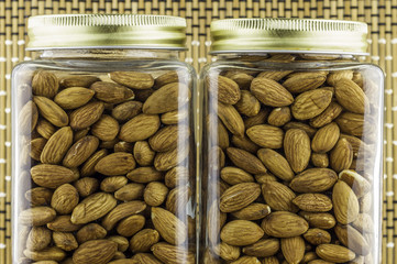 Almonds seeds pour from wood spoon on textured wooden background, top view.