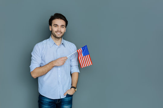 National feeling. Joyful positive patriotic man holding the US flag and smiling while being proud of his country