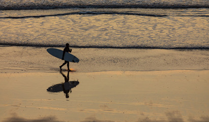 Fototapeta na wymiar Surfer walking across the beach at sunset