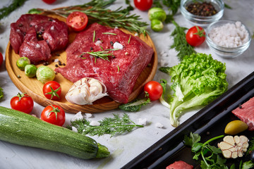 Still life of raw beef meat with vegetables on wooden plate over white background, top view, selective focus