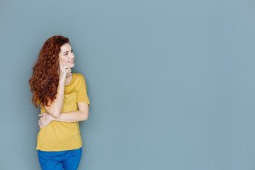 Being thoughtful. Cheerful delighted nice woman smiling and looking aside while touching her cheek