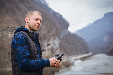 young man looking at a navigator gps on the bank of a mountain river during an extreme journey