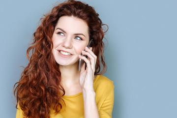 Interesting conversation. Delighted positive nice woman smiling and talking to the phone while being in a good mood