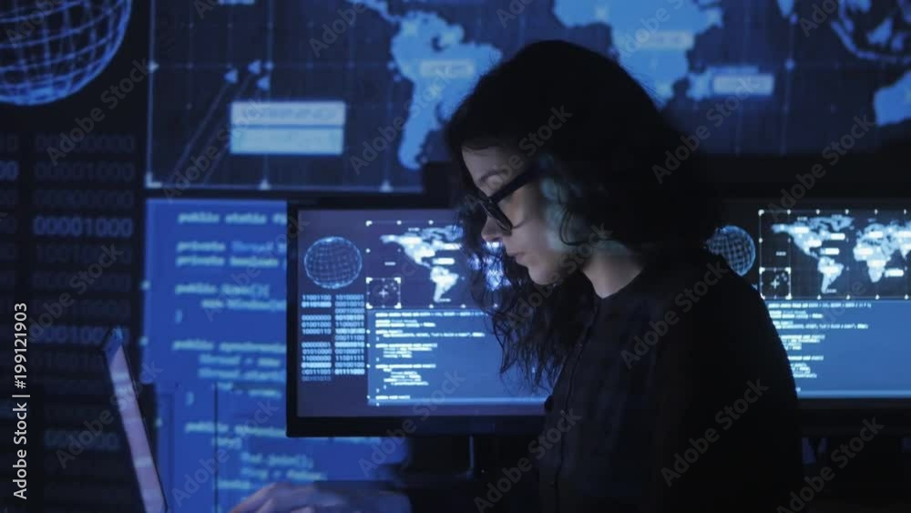 Wall mural portrait of young woman programmer in eyeglasses working at a computer in the data center filled wit