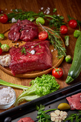 Still life of raw beef meat with vegetables on wooden plate over vintage background, top view, selective focus