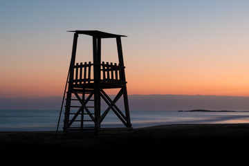 A lifeguard tower silhouette against a sunset