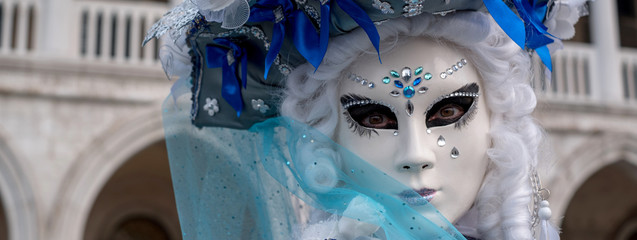 Close up of woman in ornate blue and white costume, hat and mask at the Doges Palace, St Mark's Square (Palazzo Ducale San Marco) during the Carnival (Carnival di Venezia)