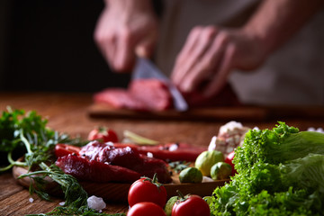 Strong professional man's hands cutting raw beefsteak, selective focus, close-up