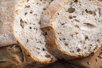 Loaves of gray bread with seeds, in a paper bag, lie on a black table made of wood.