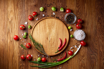Various vegetables, seasoning and spicies around blank plate on rustic wooden background, top view