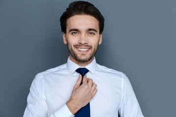 Business style. Nice joyful handsome businessman smiling and looking at you while fixing his tie