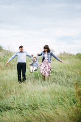 Daughter holds hands mom and dad. Hands in the hands. A young family is walking with a little daughter in the outdoors along the green grass. Happy family together. 