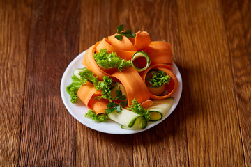 Artistically served vegetable salad with carrot, cucumber, letucce over wooden background, selective focus