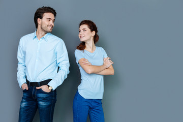 Young couple. Positive happy delighted people turning their heads and looking at each other while standing against grey background