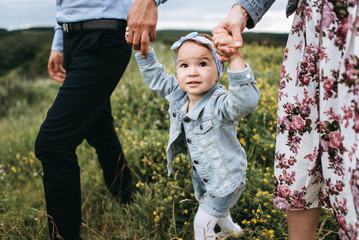 Daughter holds hands mom and dad. Hands in the hands. A young family is walking with a little daughter in the outdoors along the green grass. Happy family together. 