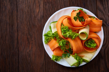 Artistically served vegetable salad with carrot, cucumber, letucce over wooden background, selective focus