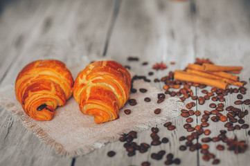 black coffee with croissants on a lined napkin sprinkled with cinnamon and anise on a light wooden table