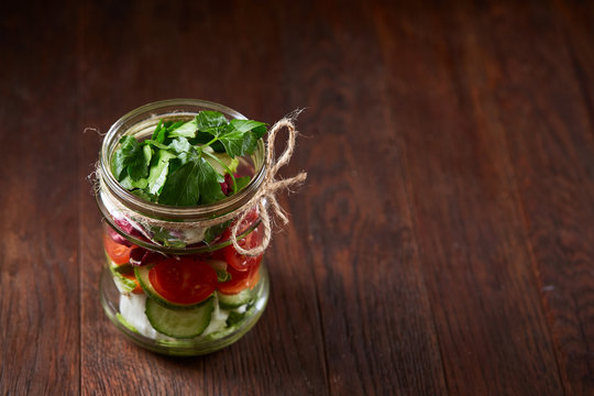 Creative vegetable salad served in glass jar over dark wooden background, selective focus, shallow depth of field