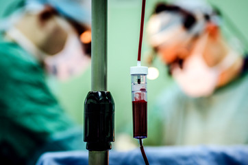 Surgeons during the operation on the background of a dropper with blood.
